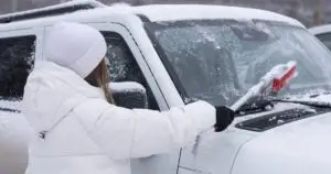 Woman scraping ice and snow from windshield of car