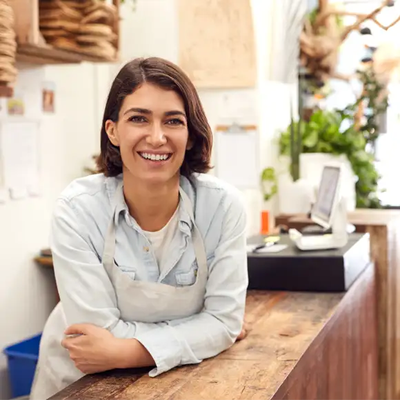 Confident female business owner standing at the checkout counter of her store, smiling