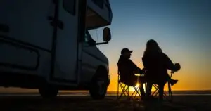 Two people sitting in front of an RV at sunset